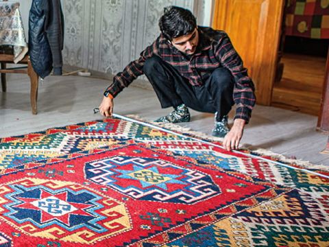 reWoven coordinator Zaur Khalilov measures the final dimensions of a recently completed rug woven by Suraya Memisova at her home.