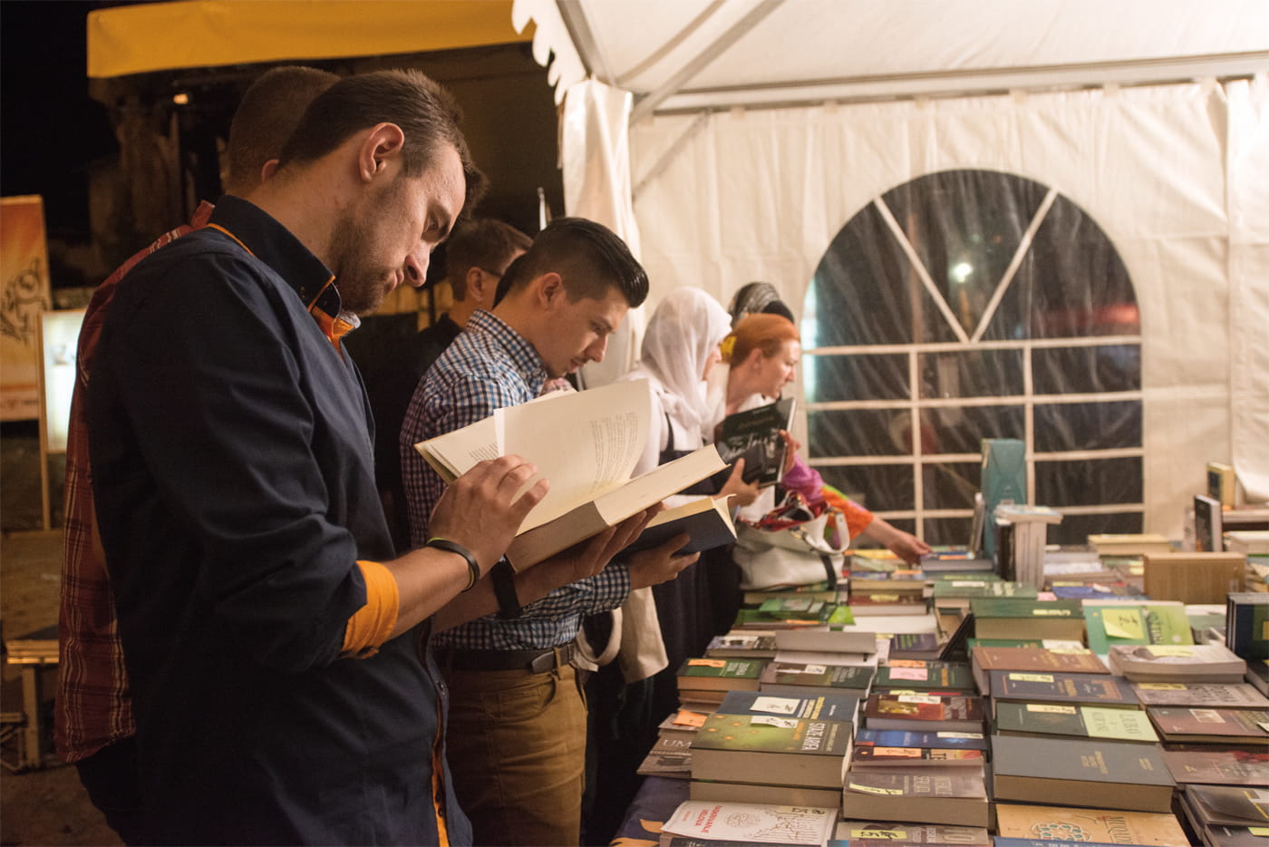 <p><em>Acima</em>: Sarajevo mantém-se como uma cidade de bibliófilos. Aqui, moradores e visitantes exploram uma feira de livros durante o Ramadã. <em>Abaixo à direita</em>: lembranças turísticas brilham na vitrine de uma loja do <em>bezistan</em> (bazar) no Baščaršija, centro comercial e cultural de Sarajevo.</p>
